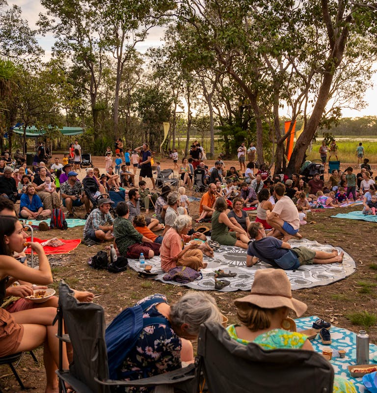 a crowd sitting on the ground outside as the sunsets